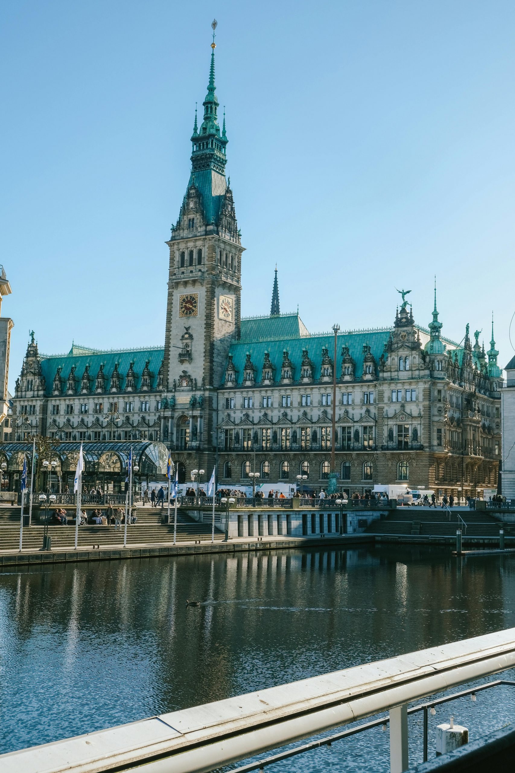 A scenic view of Hamburg City Hall with a clear blue sky and Alster River reflection.